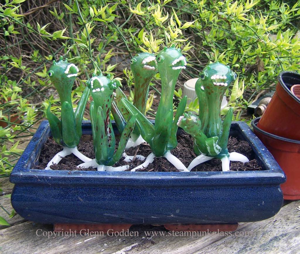 Group of green baby triffid plants, made of glass bu flameworking, with tripod base of white roots